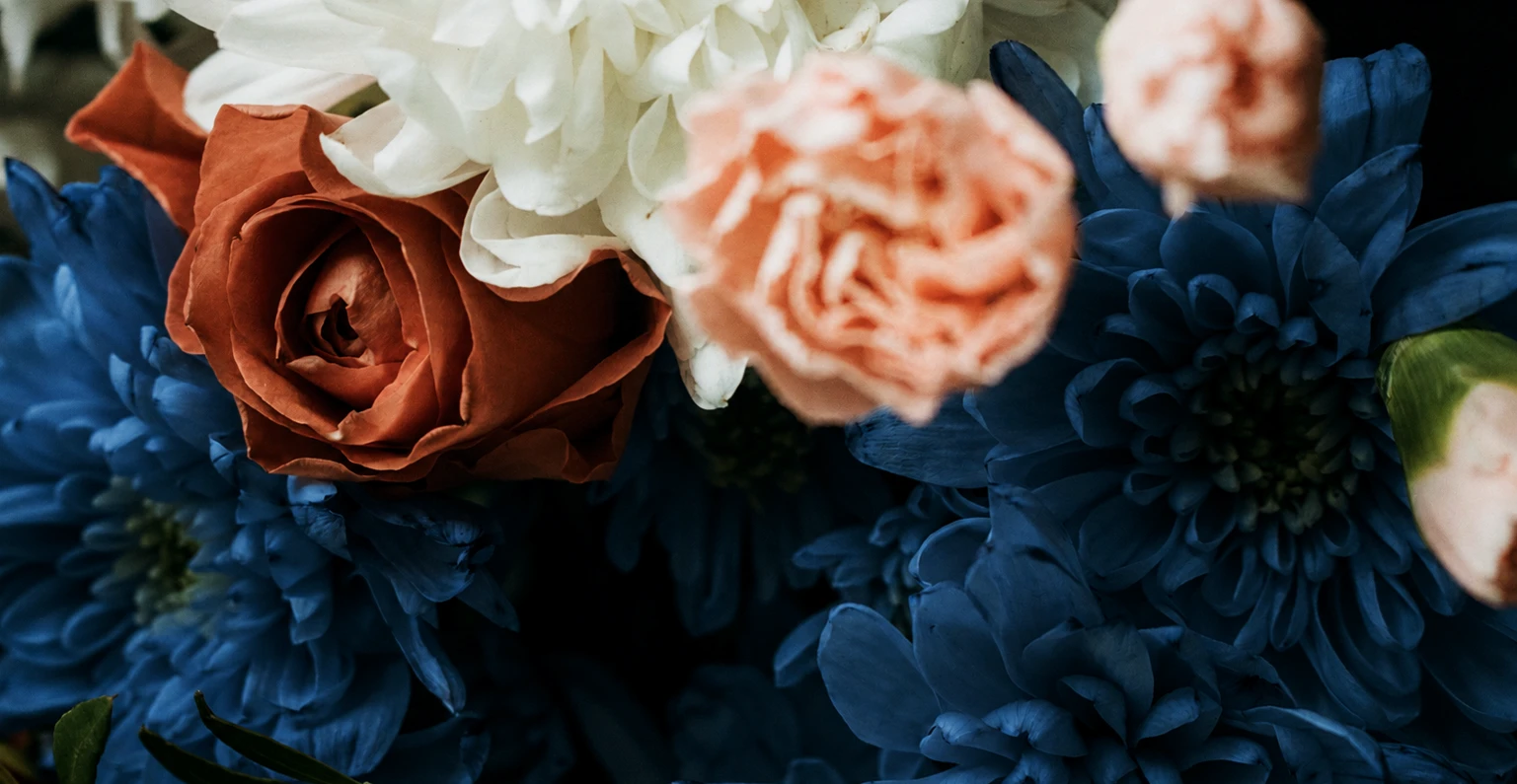 Composición floral con rosas terracota, flores azules y crisantemos blancos