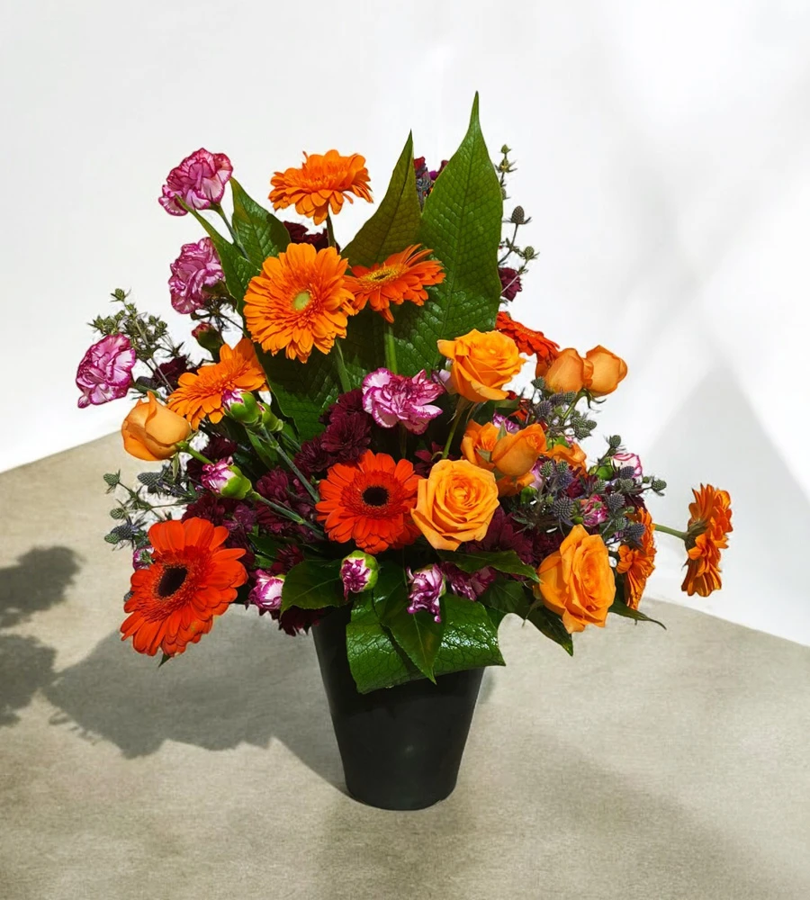 Arreglo floral en tonos naranjas, rosas y morados en base negra